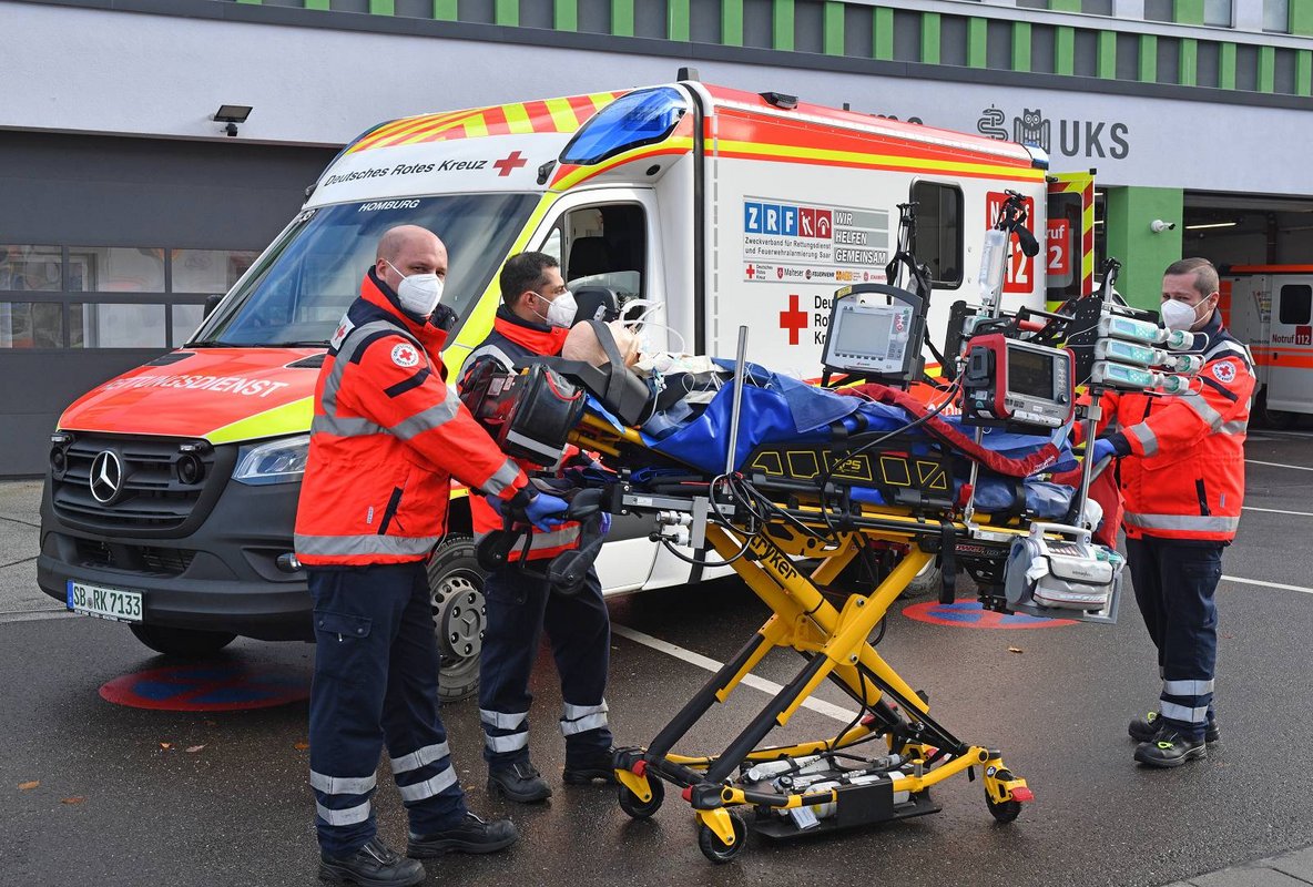 Emergency medical team transporting a patient with intensive-care equipment beside an ambulance.
